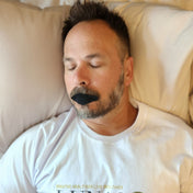 A man sleeping soundly while wearing Lunasol Sleep Just the Lips Mouth Tape in Eclipse Black, promoting nasal breathing for improved sleep quality and overall health.